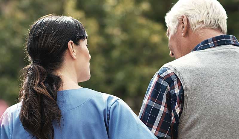 Caregiver assisting elderly man outdoors